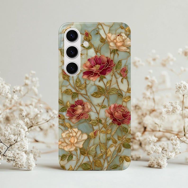 May include: A phone case featuring a floral design with red, pink, and cream-colored roses. The roses are set against a light blue background with gold-colored accents. The case has a glossy finish and a camera cutout.