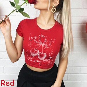 May include: A red crop top with a white graphic of two cherries, a bow, and the words "Love you" and "cherry much". The shirt has short sleeves and a round neckline. The word "Red" is at the bottom left.