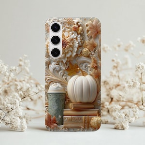 May include: A phone case featuring a detailed relief design with a fall theme. The design includes a white pumpkin, books, leaves, and floral elements in shades of cream, gold, and beige. A green cup with a white topping is also visible.