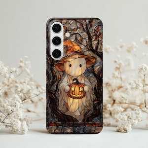 Puede incluir: Funda de teléfono con un diseño de vidriera de una figura de Halloween sosteniendo una calabaza brillante. La figura lleva un sombrero marrón y una túnica blanca, enmarcada por ramas oscuras y hojas de otoño.