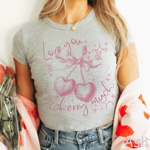 May include: A gray t-shirt with a pink cherry graphic and the words "Love you cherry much". The design includes two cherries, a bow, and starbursts. The shirt is a cropped style.
