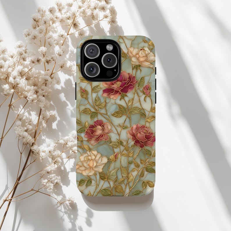May include: A phone case featuring a floral design with red and cream roses, green leaves, and gold-colored stems on a light blue background. The case has a glossy finish and a camera cutout.