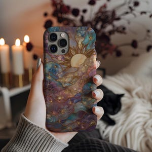 Puede incluir: Funda de tel&eacute;fono colorida con un dise&ntilde;o celestial que presenta un sol, estrellas y nubes en tonos azules, morados y dorados. La funda tiene un acabado brillante.