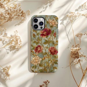 May include: A smartphone case featuring a floral design with red and cream-colored roses, green leaves, and gold-colored stems. The case has a light blue background and a glossy finish. The case has a camera cutout and buttons.