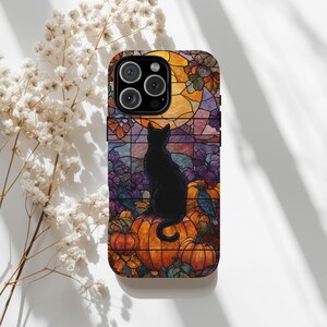 May include: A phone case featuring a stained-glass design with a black cat sitting on pumpkins. The background includes a full moon, fall foliage, and a raven. The case has a colorful, autumnal theme.