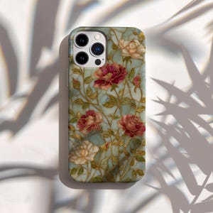 May include: A phone case featuring a floral design with red and cream-colored roses, green leaves, and gold-colored stems against a light blue background. The case has a glossy finish and a camera cutout.