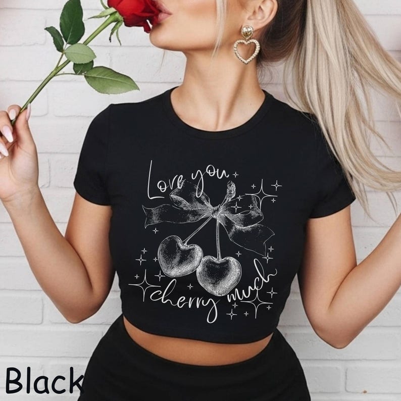 May include: Black crop top with a white graphic of two cherries tied with a bow and the words "Love you cherry much". The shirt has short sleeves and a round neckline. The word "Black" is printed at the bottom left.