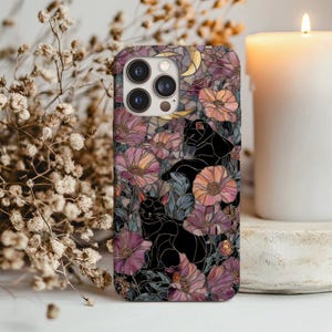 May include: A phone case featuring a floral design with black cat silhouettes, pink and peach flowers, and a crescent moon. The case has a glossy finish and a camera cutout.