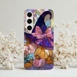Puede incluir: Funda de teléfono con diseño de vidriera que representa un sombrero de bruja, un gran lazo rosa y calabazas en tonos naranja, rosa y amarillo. El fondo es morado y azul con hojas de otoño.