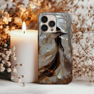 Puede incluir: Funda de teléfono con diseño de bruja. La funda tiene un fondo nacarado con una bruja con un vestido largo y sombrero, sosteniendo una escoba. La bruja camina por un bosque con árboles desnudos y hojas caídas. La funda tiene un módulo de cámara con tres lentes.