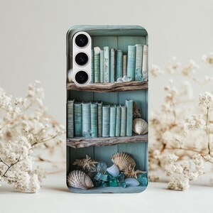 May include: A phone case featuring a teal bookshelf design with vintage books, seashells, and sea glass. The case has a three-lens camera cutout and a light-colored background with white flowers.