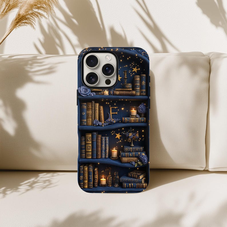 May include: A navy blue phone case featuring a bookshelf design with books, candles, and floral accents. The letter "F" is visible on the middle shelf. The case has a glossy finish and a dark blue border.