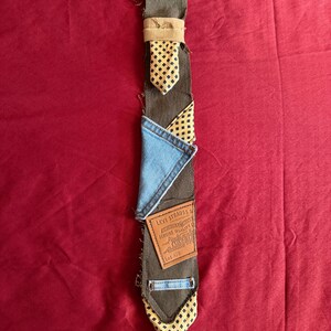 May include: A necktie constructed from olive green fabric featuring a patchwork design. It includes a yellow and black diamond-patterned fabric, a light blue denim triangle, and a brown leather Levi Strauss & Co. patch with visible text.