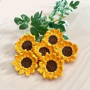 May include: Six crocheted sunflower decorations in yellow and brown. The sunflowers are arranged in a cluster, with the centers facing outwards.