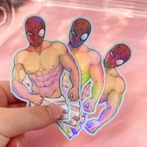 May include: Three holographic stickers featuring a muscular figure wearing a red and black spider-patterned mask. The figure is shirtless, showing defined abdominal muscles, and is wrapped in a white towel around the waist with a rainbow sheen.