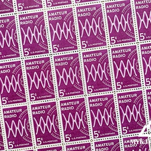 May include: A sheet of vintage 5-cent U.S. postage stamps. Each stamp is a deep purple with the words "AMATEUR RADIO" and a stylized wave design in white. The stamps are arranged in a grid pattern.