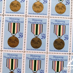 May include: A sheet of postage stamps featuring a military medal design. Each stamp has a light blue background with the text "Honoring Those Who Served" and "USA 29". The medal has a ribbon with red, white, green, and blue stripes.
