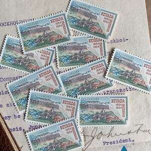 K&ouml;nnte beinhalten: Eine Sammlung von Vintage-US-Briefmarken mit dem Bundesstaat Nevada. Die Briefmarken sind blau, gr&uuml;n und rot mit dem Text "Nevada Statehood 1864 1964" auf jeder Marke.