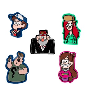 May include: Five colorful cartoon character pins featuring characters from the animated series Gravity Falls. The pins are of Stan Pines, Mabel Pines, Dipper Pines, Wendy Corduroy, and Soos.