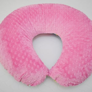 May include: A pink pregnancy pillow with a textured surface. The pillow is shaped like a horseshoe and is designed to provide support for pregnant women.