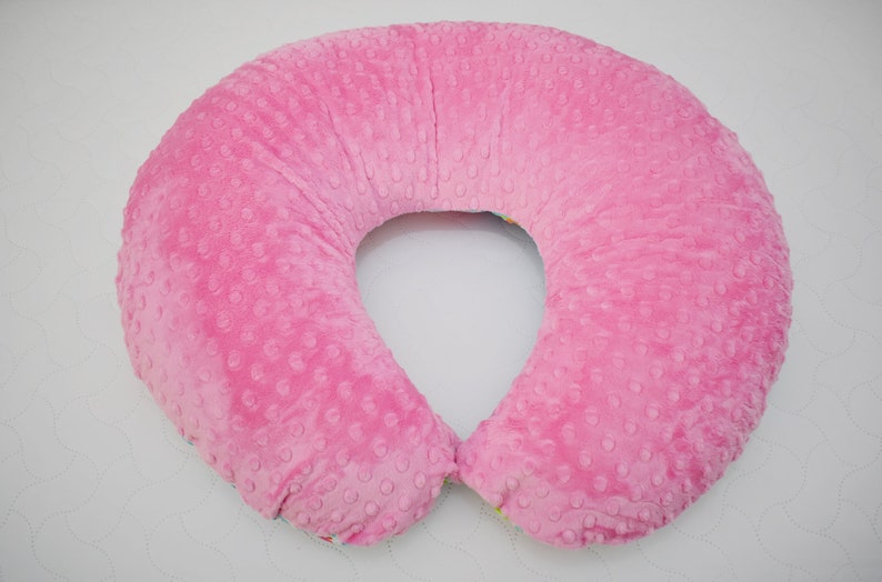 May include: A pink pregnancy pillow with a textured surface. The pillow is shaped like a horseshoe and is designed to provide support for pregnant women.