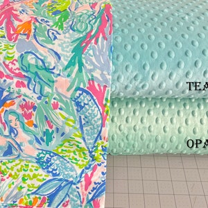 May include: Two fabric swatches, one with a mermaid and coral reef pattern in shades of blue, green, pink, and orange, and the other a solid teal minky fabric with a subtle dot pattern. The text "TEAL" is printed on the teal fabric and "OPAL" is printed on the green fabric.