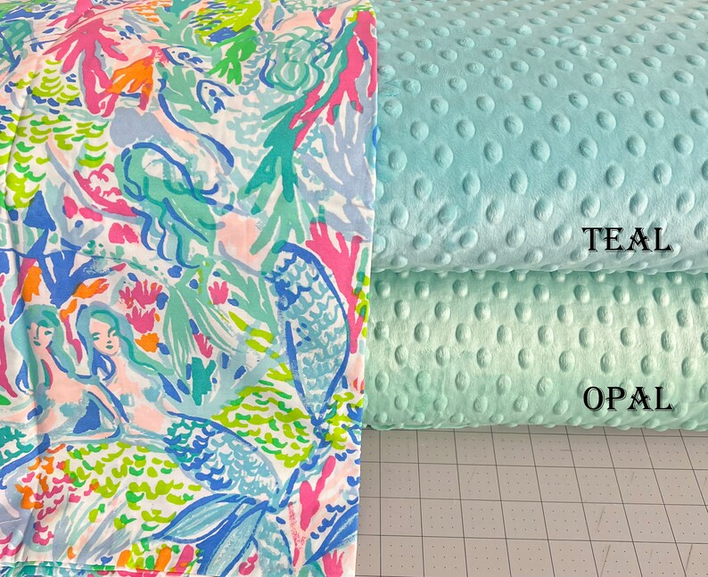 May include: Two fabric swatches, one with a mermaid and coral reef pattern in shades of blue, green, pink, and orange, and the other a solid teal minky fabric with a subtle dot pattern. The text "TEAL" is printed on the teal fabric and "OPAL" is printed on the green fabric.