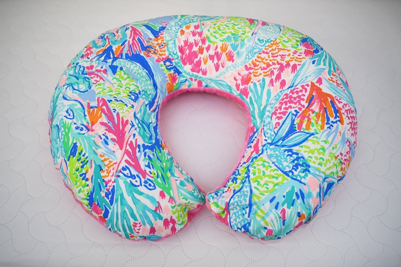 May include: A pink and white patterned pregnancy pillow with a U-shape design. The pillow is covered in a floral print with pink, blue, green, and orange colors.