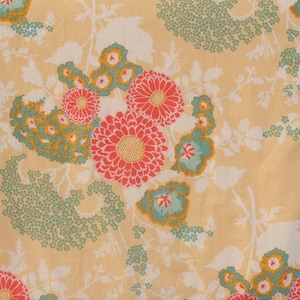 May include: A beige fabric with a floral pattern. The flowers are red, pink, and blue with green leaves. The background is a light beige.