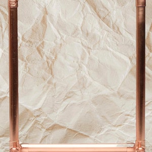 May include: A copper pipe frame with two shelves. The frame is made of copper pipes and fittings. The frame is on a crumpled brown paper background.