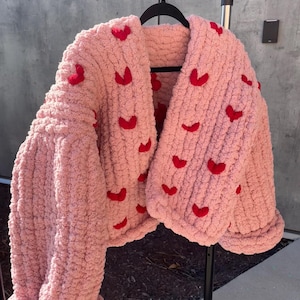 May include: A pink knitted cardigan with a V-neck and red heart embellishments.