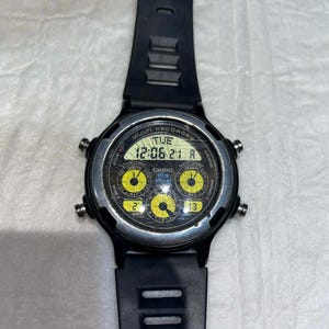 Puede incluir: Reloj digital Casio negro con correa negra. La esfera del reloj muestra la hora, la fecha y otras funciones en formato digital. El reloj tiene detalles en amarillo y varios botones.