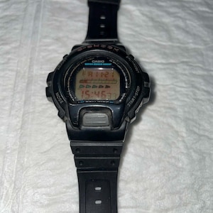Puede incluir: Reloj digital Casio G-Shock negro con correa negra. La esfera muestra la hora y la fecha. Tiene botones para ajustar el modo, iniciar/detener y dividir/restablecer. El reloj es resistente al agua.