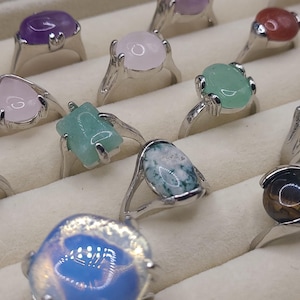 May include: A collection of rings featuring a variety of gemstone settings. The rings are made of silver and feature a variety of stones, including amethyst, rose quartz, green aventurine, agate, and tiger's eye.
