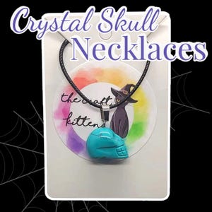 May include: A turquoise crystal skull pendant necklace. The skull is carved with detailed features and hangs from a black cord. The background includes the text "Crystal Skull Necklaces" and a colourful circular design with a black cat.