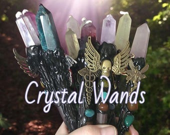 May include: A collection of crystal wands with black handles and various colored crystal tips. The wands are adorned with metal accents, including wings and a skull. The text "Crystal Wands" is visible in the image.