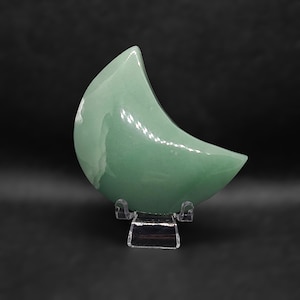 Pode incluir: Uma pedra polida em forma de lua crescente verde em um suporte de pl&aacute;stico transparente.