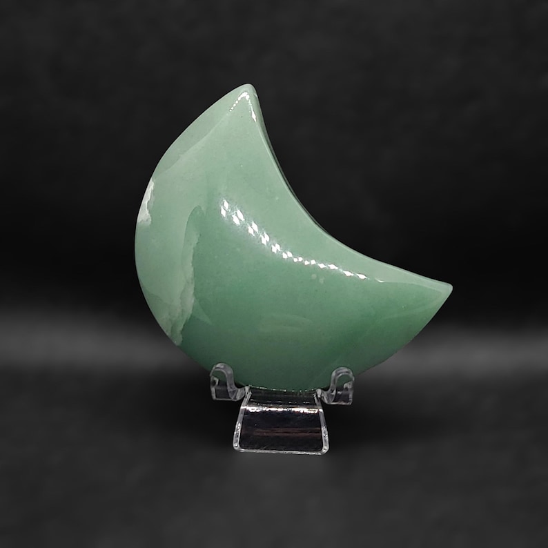 Pode incluir: Uma pedra polida em forma de lua crescente verde em um suporte de pl&aacute;stico transparente.