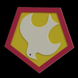 Op de afbeelding: Een decoratief embleem met een witte duif in vlucht, tegen een gele achtergrond in een rood vijfhoekig frame. De duif heeft een klein zwart oog. Het ontwerp staat tegen een zwarte achtergrond.
