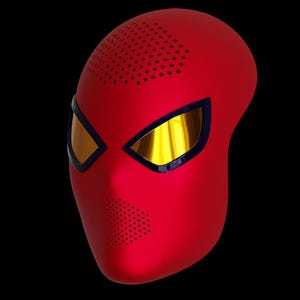 Puede incluir: Una máscara de superhéroe roja y negra con ojos dorados. La máscara tiene una superficie texturizada y un contorno negro alrededor de los ojos.