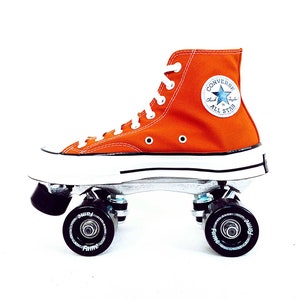 May include: Orange Converse high-top sneakers on roller skates with black wheels. The sneakers have a white sole and a blue star logo with the text "Chuck Taylor All Star".