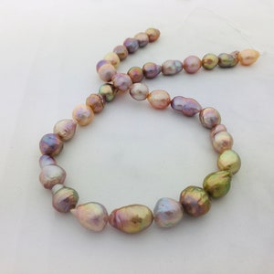 May include: A strand of iridescent pearls in shades of pink, green, and gold. The pearls are strung on a white thread and are arranged in a circle.