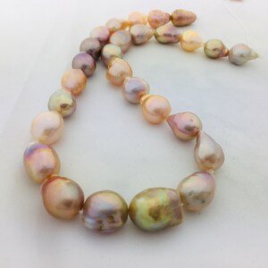 May include: A strand of iridescent pearls in shades of pink, gold, and white. The pearls are strung on a white cord and are of varying sizes and shapes.