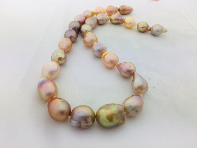 May include: A strand of iridescent pearls in shades of pink, gold, and white. The pearls are strung on a white cord and are of varying sizes and shapes.