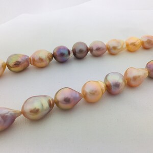 May include: A strand of baroque pearls in shades of pink, peach, and lavender. The pearls are strung on a clear thread and have an iridescent sheen.