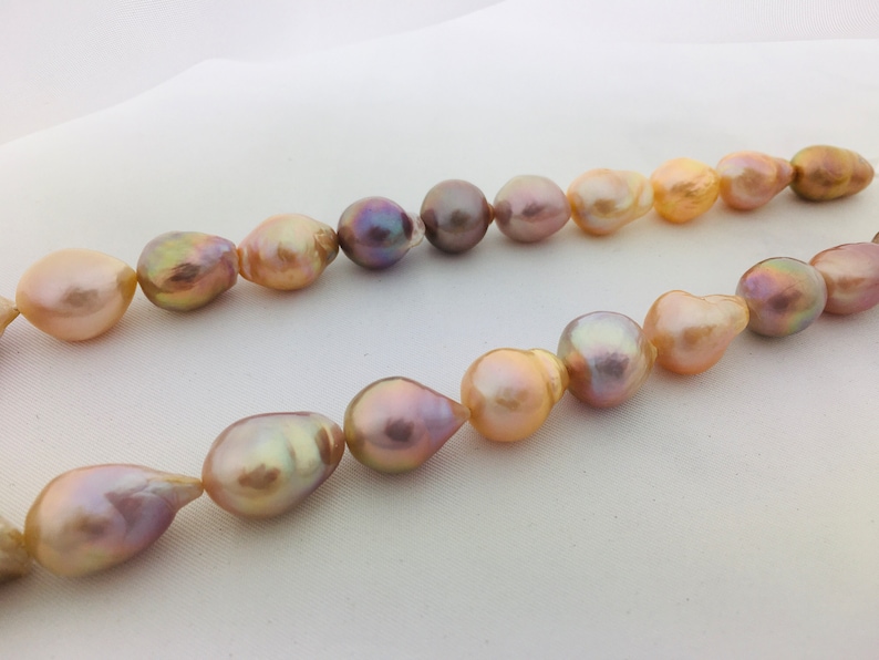 May include: A strand of baroque pearls in shades of pink, peach, and lavender. The pearls are strung on a clear thread and have an iridescent sheen.