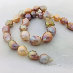May include: A strand of iridescent baroque pearls in shades of pink, gold, and white. The pearls are strung on a white thread and are ready to be made into a necklace or bracelet.