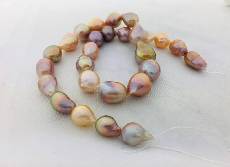 May include: A strand of iridescent baroque pearls in shades of pink, gold, and white. The pearls are strung on a white thread and are ready to be made into a necklace or bracelet.