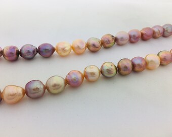 May include: A strand of baroque pearls in shades of pink, peach, and cream. The pearls are strung on a clear thread and are of varying sizes.