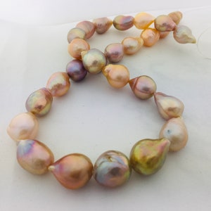 May include: A strand of iridescent baroque pearls in shades of pink, gold, and purple. The pearls are strung on a white thread and are arranged in a circular pattern.